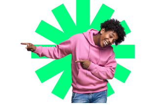 Junger Mann im rosa Hoodie zeigt lachend zur Seite.